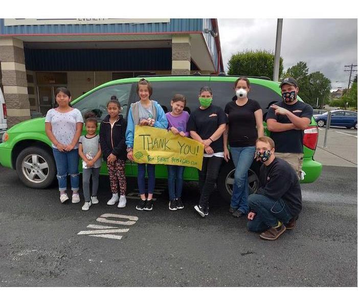 children and adults standing in front of a green SERVPRO van